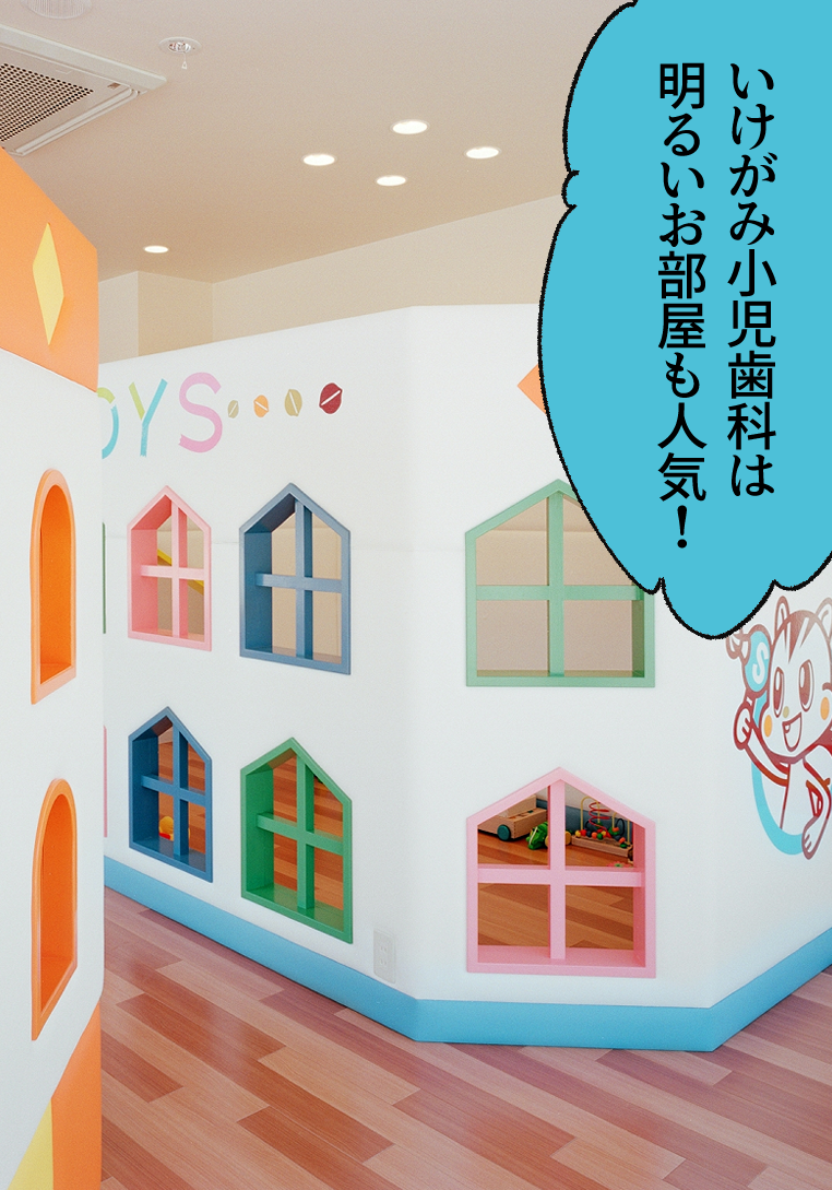 アッキー「いけがみ小児歯科は明るいお部屋も人気!」背景にいけがみ小児歯科の待合室。室内は明るく、カラフルな家型の飾り窓が並ぶ width=